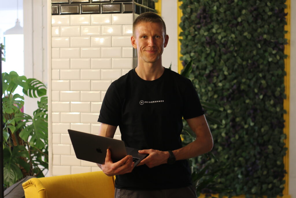 Zbynek, a white man in a black "primehammer" t-shirt, poses for a photo while holding his laptop.
