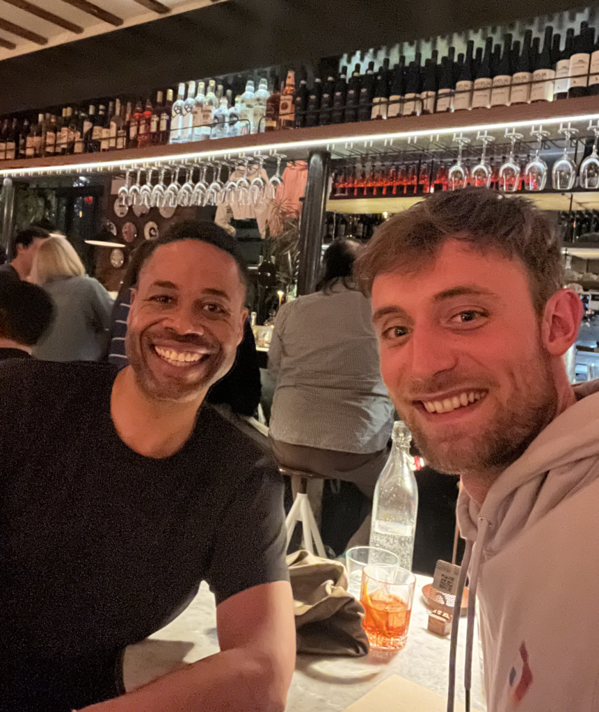 Daniel and his client smiling for a selfie in a restaurant, while sitting at a table.